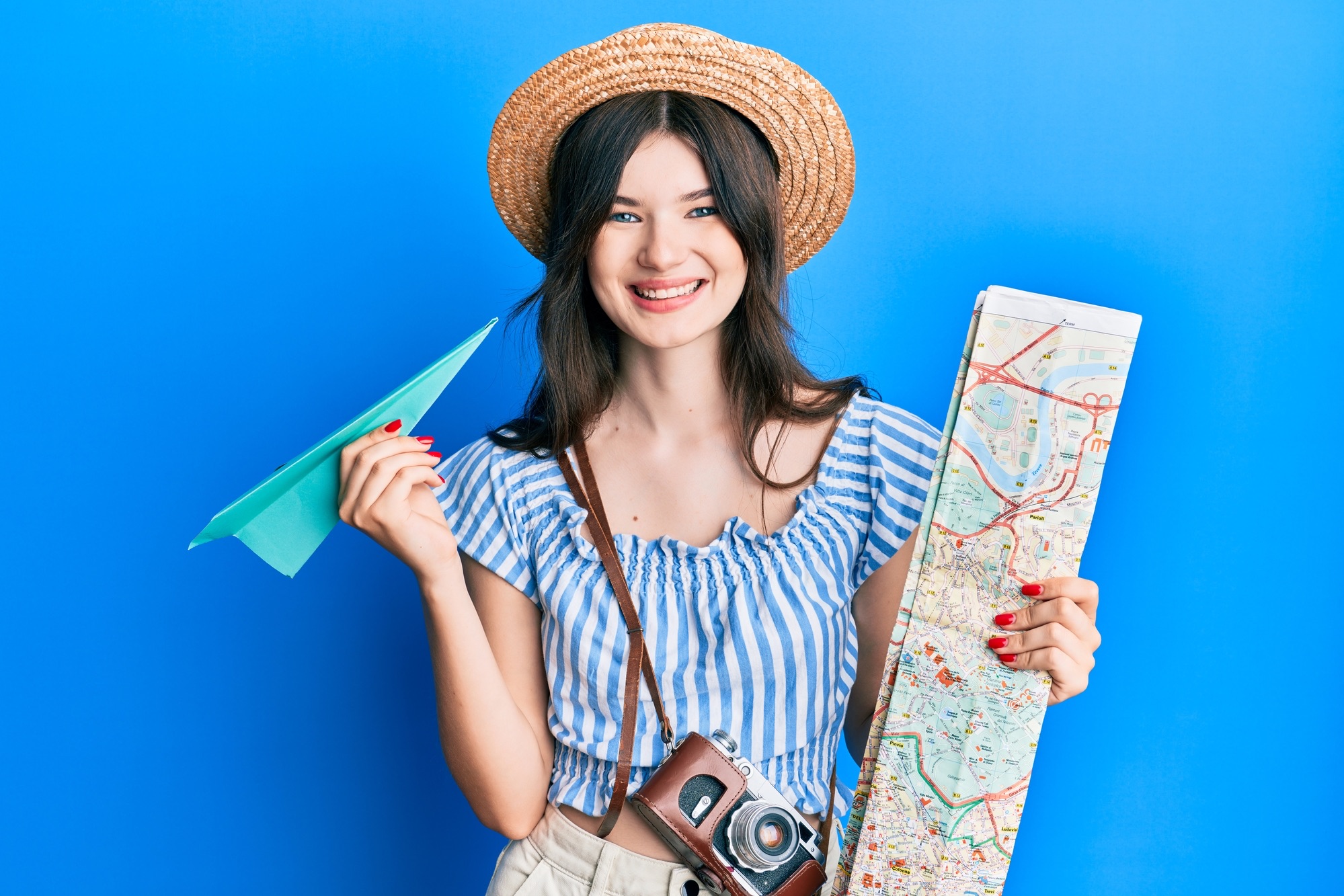 Young beautiful caucasian girl holding paper plane and city map smiling with a happy and cool smile on face. showing teeth.