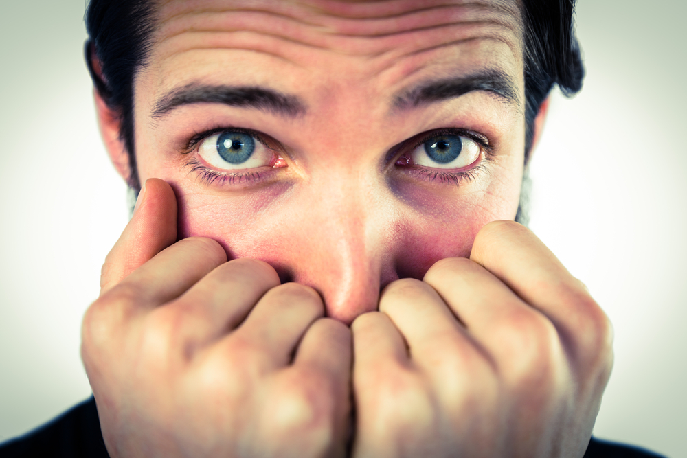 Scared hipster with hands to face on vignette background