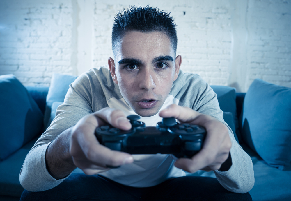 Portrait of young student man playing video games at night using wireless remote joystick with freak intense addicted face having fun in Male game addiction to console play station and video.