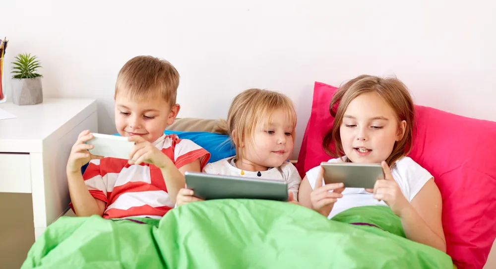 childhood, technology and family concept - little kids with tablet pc computer and smartphones in bed at home