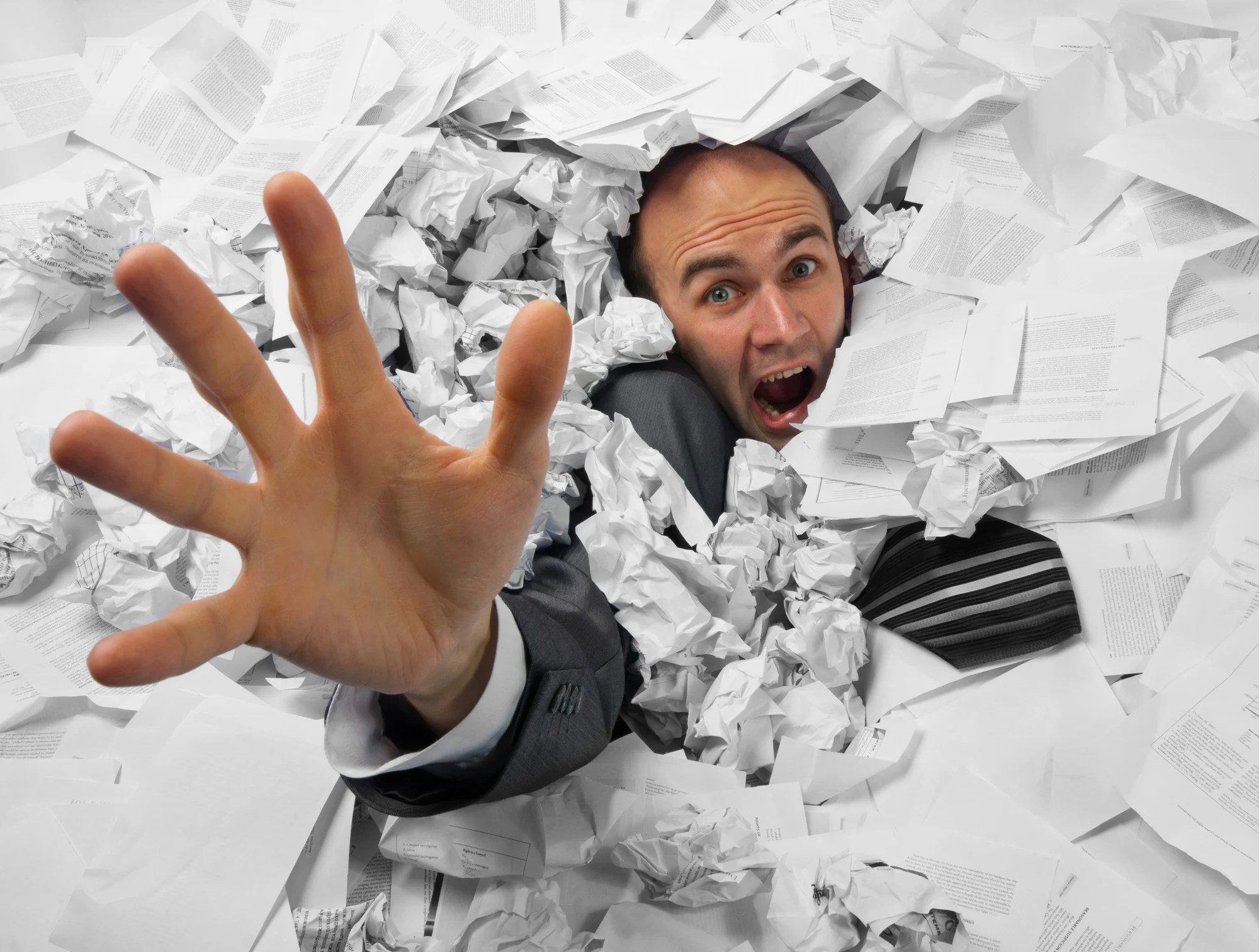 Businessman sinking in heap of documents and asking for help.