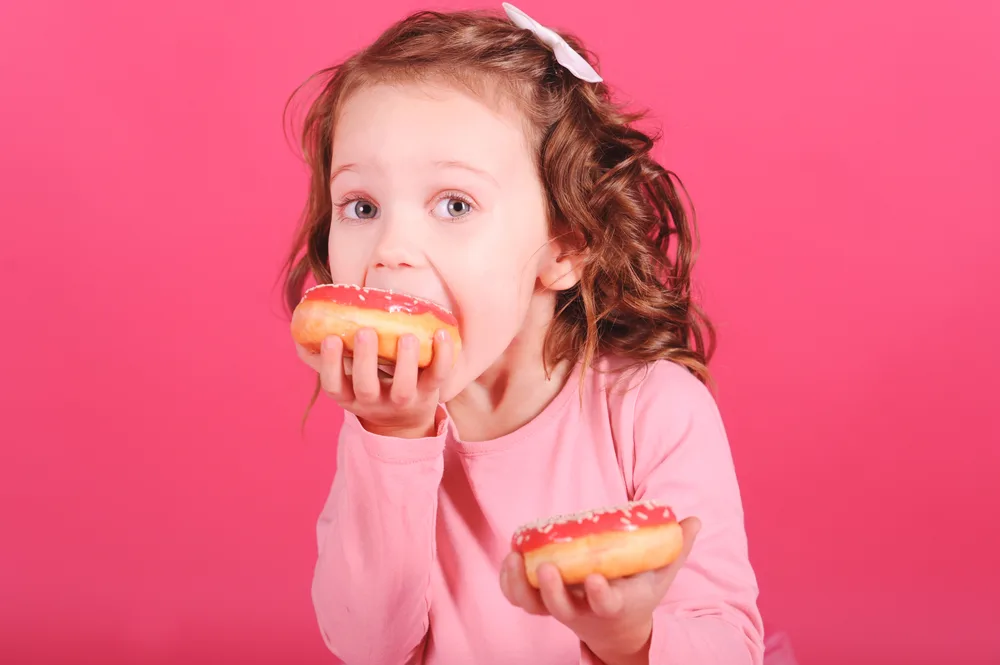 Cute,Baby,Girl,Eating,Sweet,Donuts,Over,Pink,Background