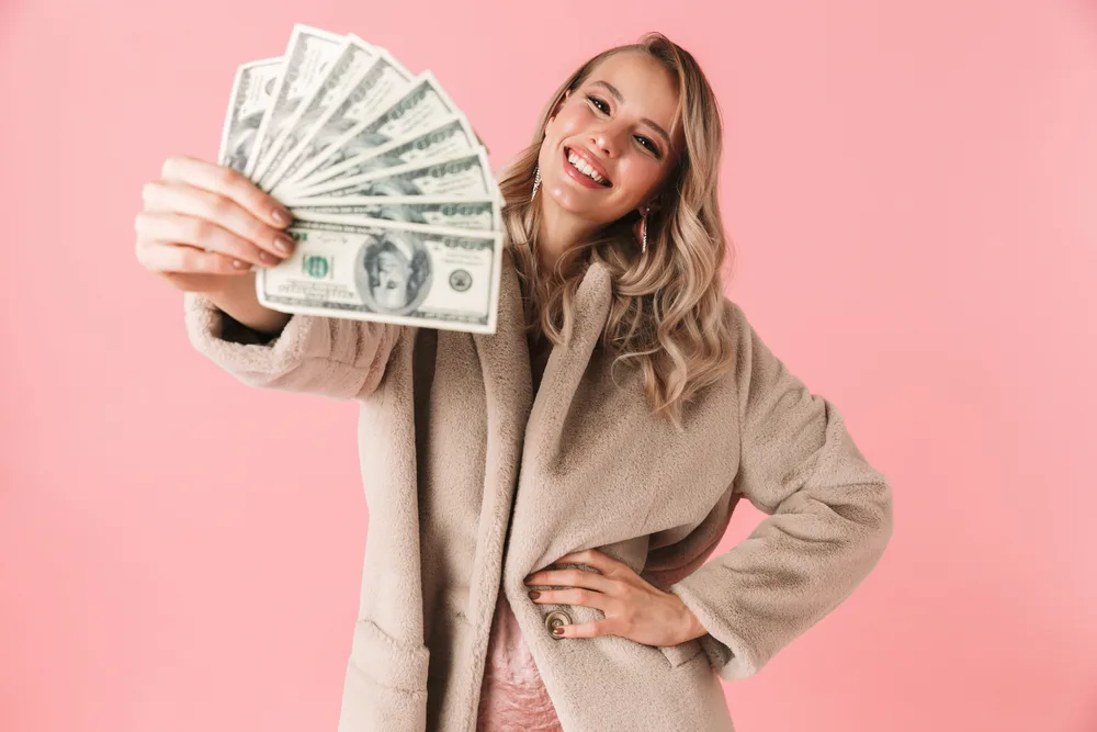 Image of a beautiful young pretty woman posing isolated over pink wall background holding money.