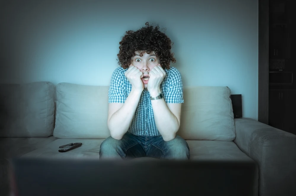 Man is watching thriller or horror on TV.