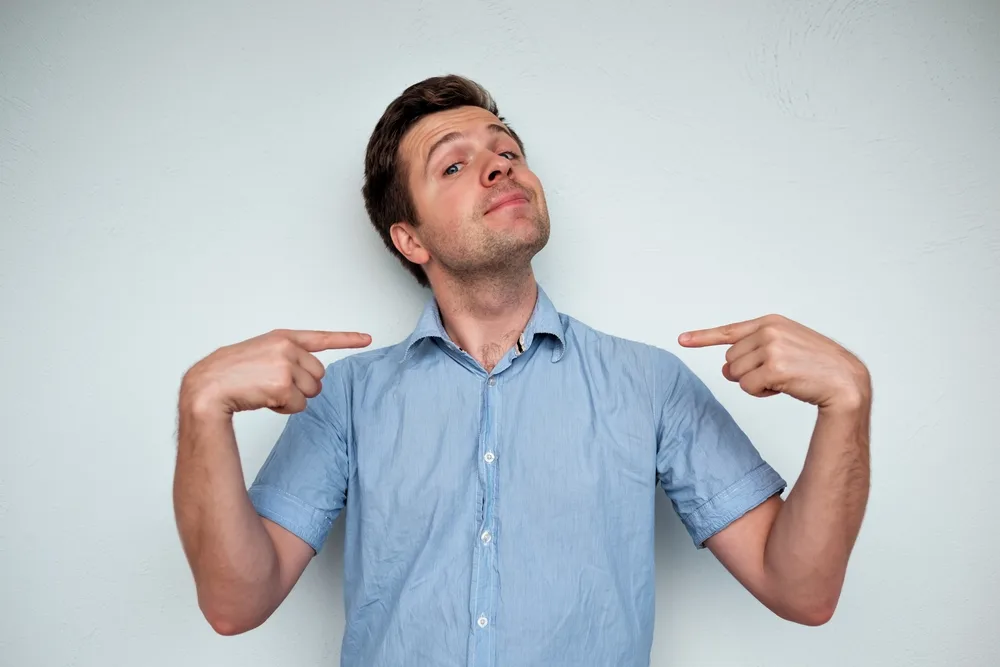 Self-satisfied and proud caucasian young man looks forward showing with index fingers on himself