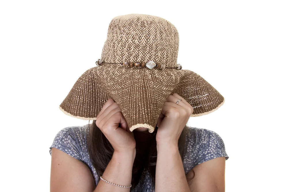 A beautiful and shy thirty something woman wearing a hat.