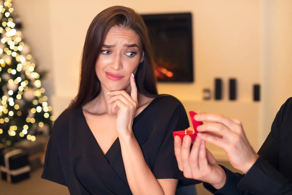 Proposal Failure. Confused young woman in doubt looking at engagement ring, man giving open box, uninterested shocked lady saying no. Negative Reaction to Proposing. Disappointment Concept.