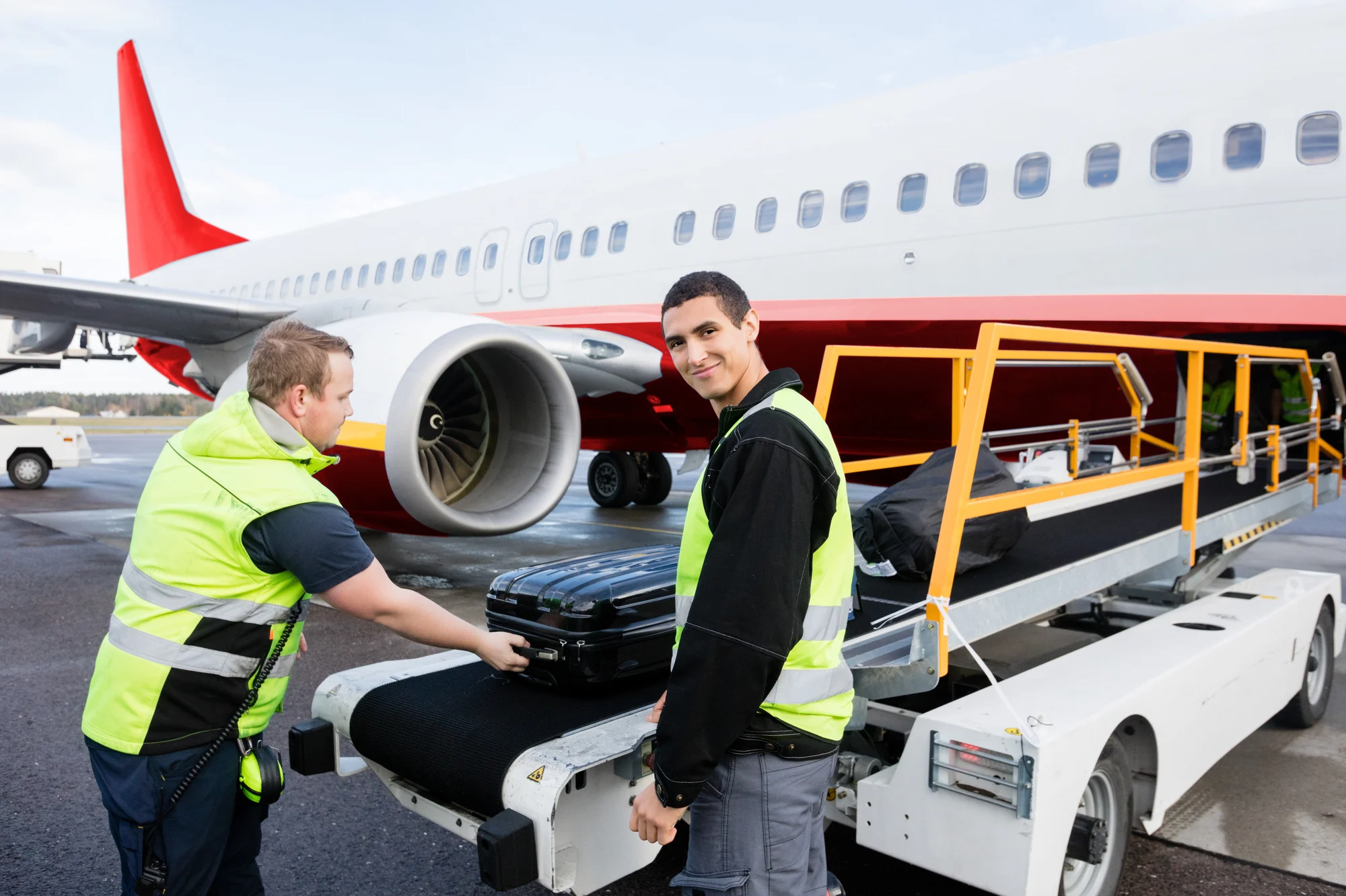 Portrait of confident worker smiling while colleague unloading luggage on runway