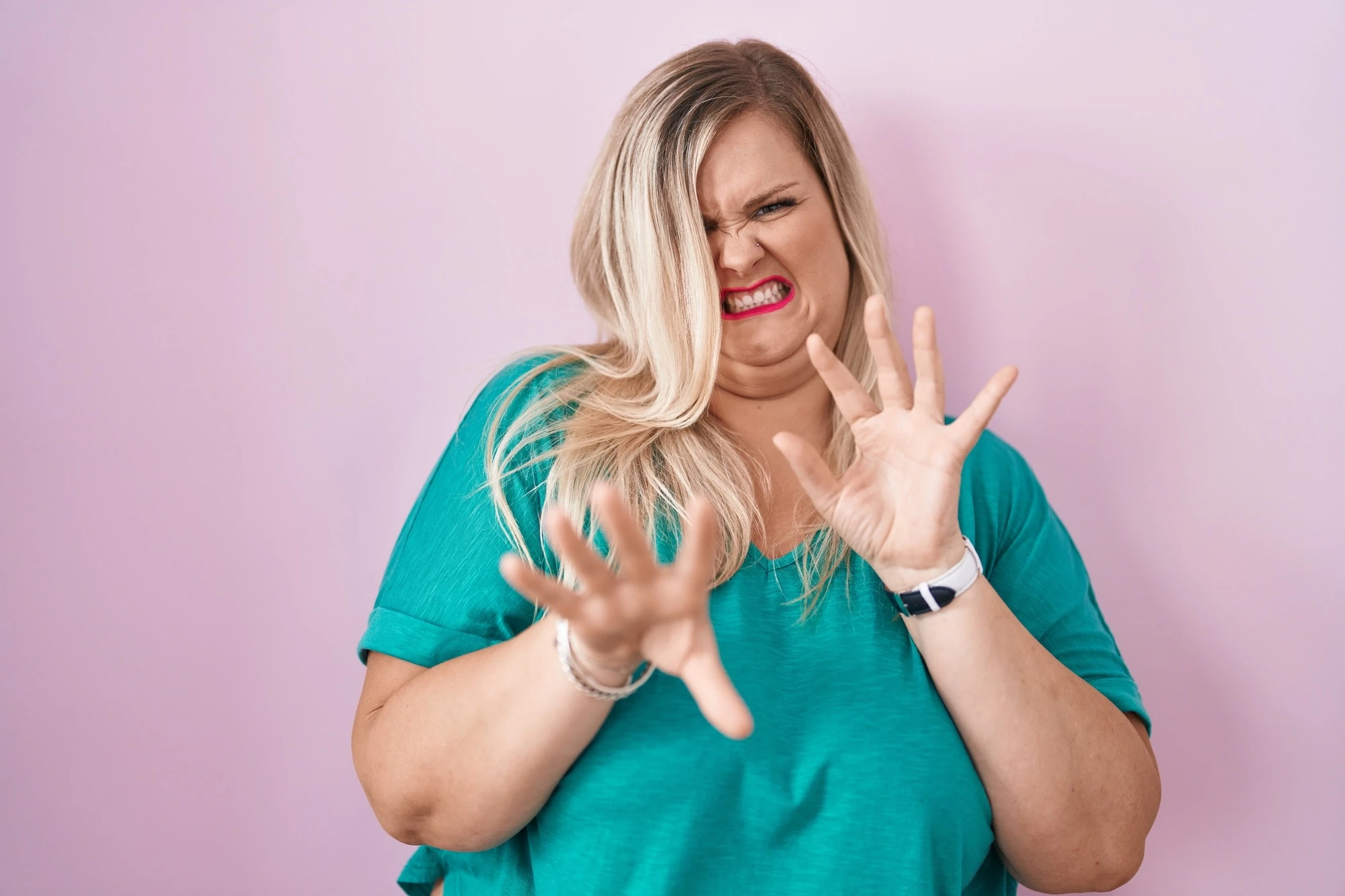 Caucasian plus size woman standing over pink background disgusted expression, displeased and fearful doing disgust face because aversion reaction.