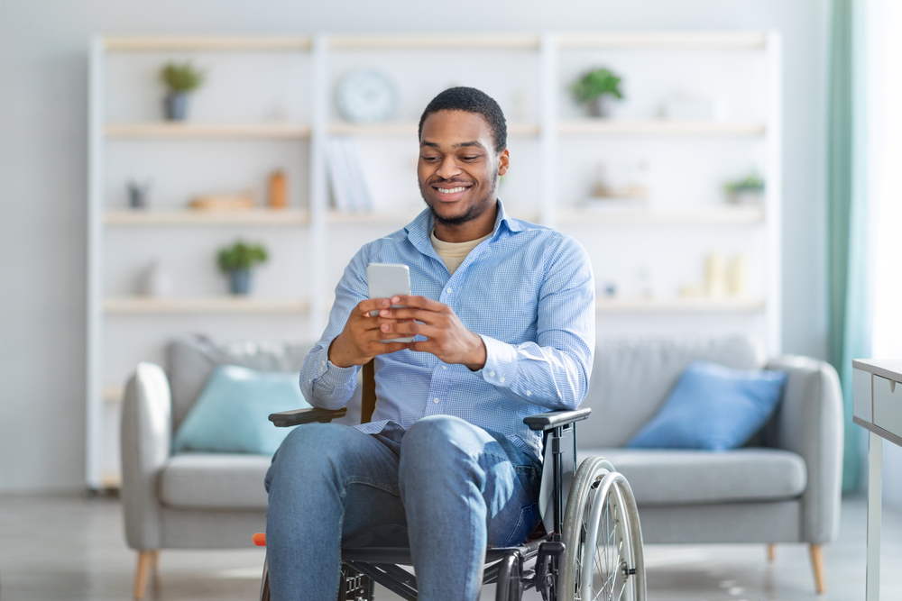 Disabled,Black,Man,In,Wheelchair,Using,Smartphone,,Browsing,Web,Or