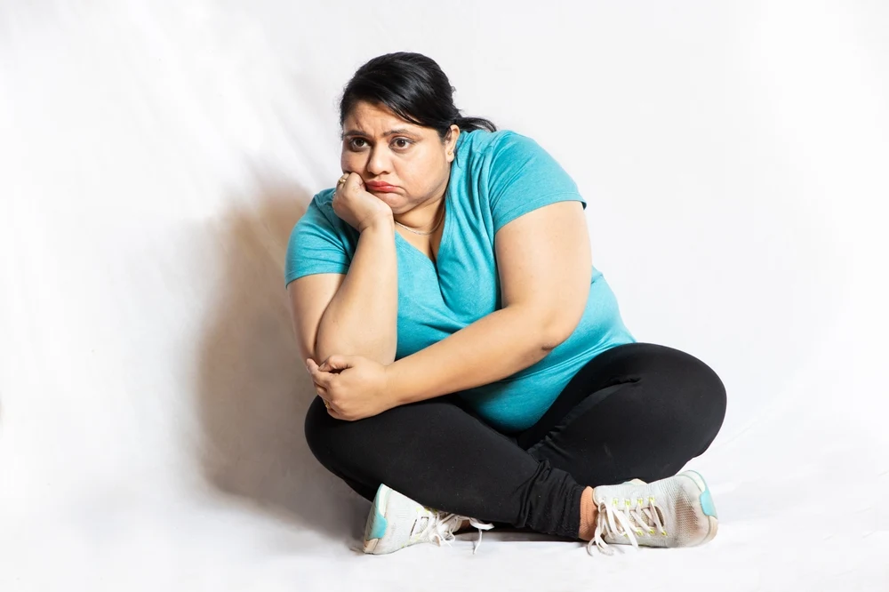 Sad,Overweight,Indian,Woman,Sitting,On,Floor,Isolated,Over,White