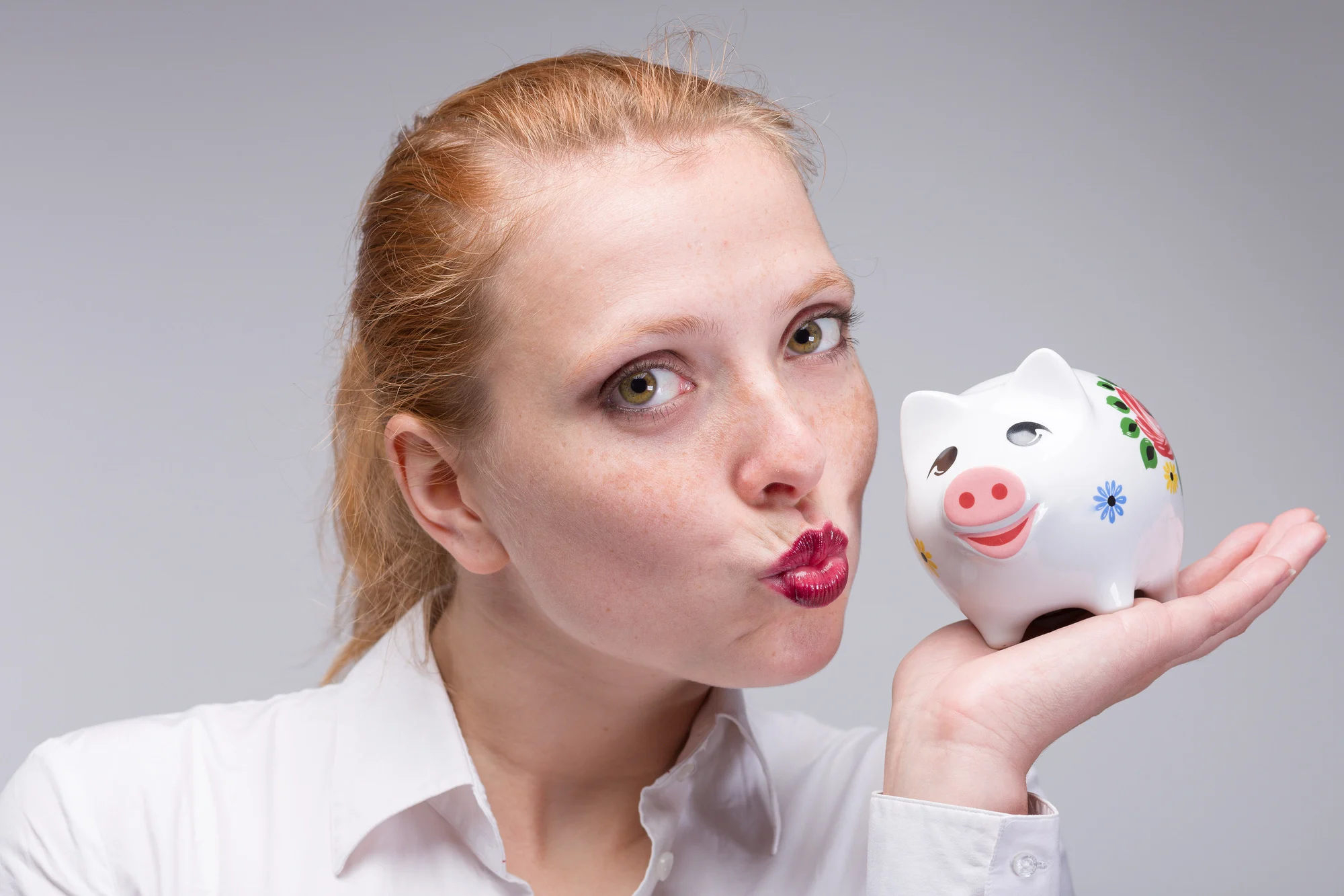 young red haired woman puts a coin into her piggy bank / porcelain bank