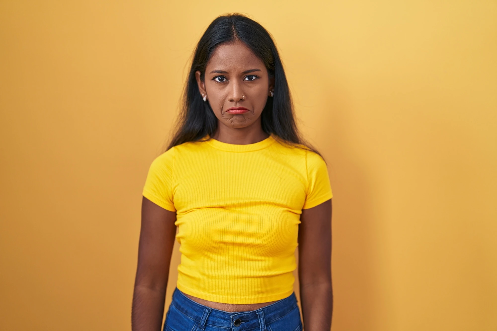 Young indian woman standing over yellow background depressed and worry for distress, crying angry and afraid. sad expression.