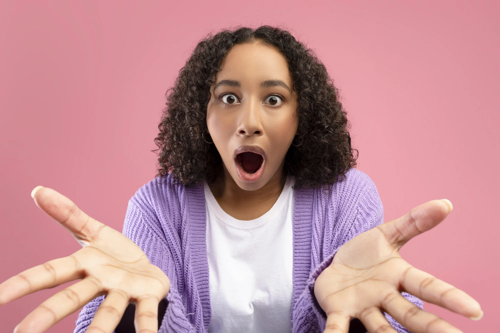 Shocked black woman looking at camera with open mouth, expressing amazement on pink studio background. Millennial African American lady feeling surprised, receiving unexpected news