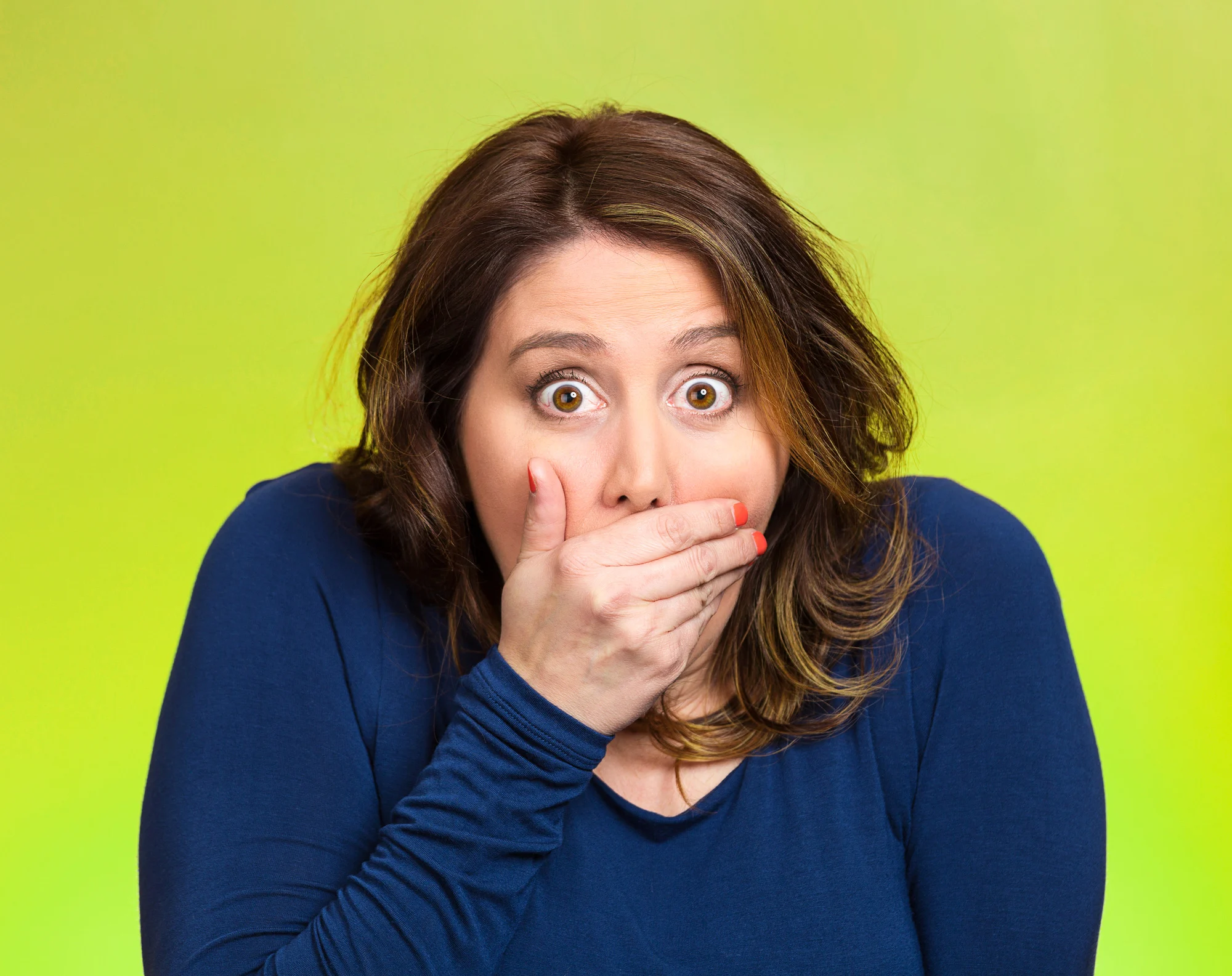 Closeup portrait middle aged shocked young woman, covering her mouth, wide open eyes, isolated green background. Negative human emotion, facial expression, feeling, signs, symbol, reaction.