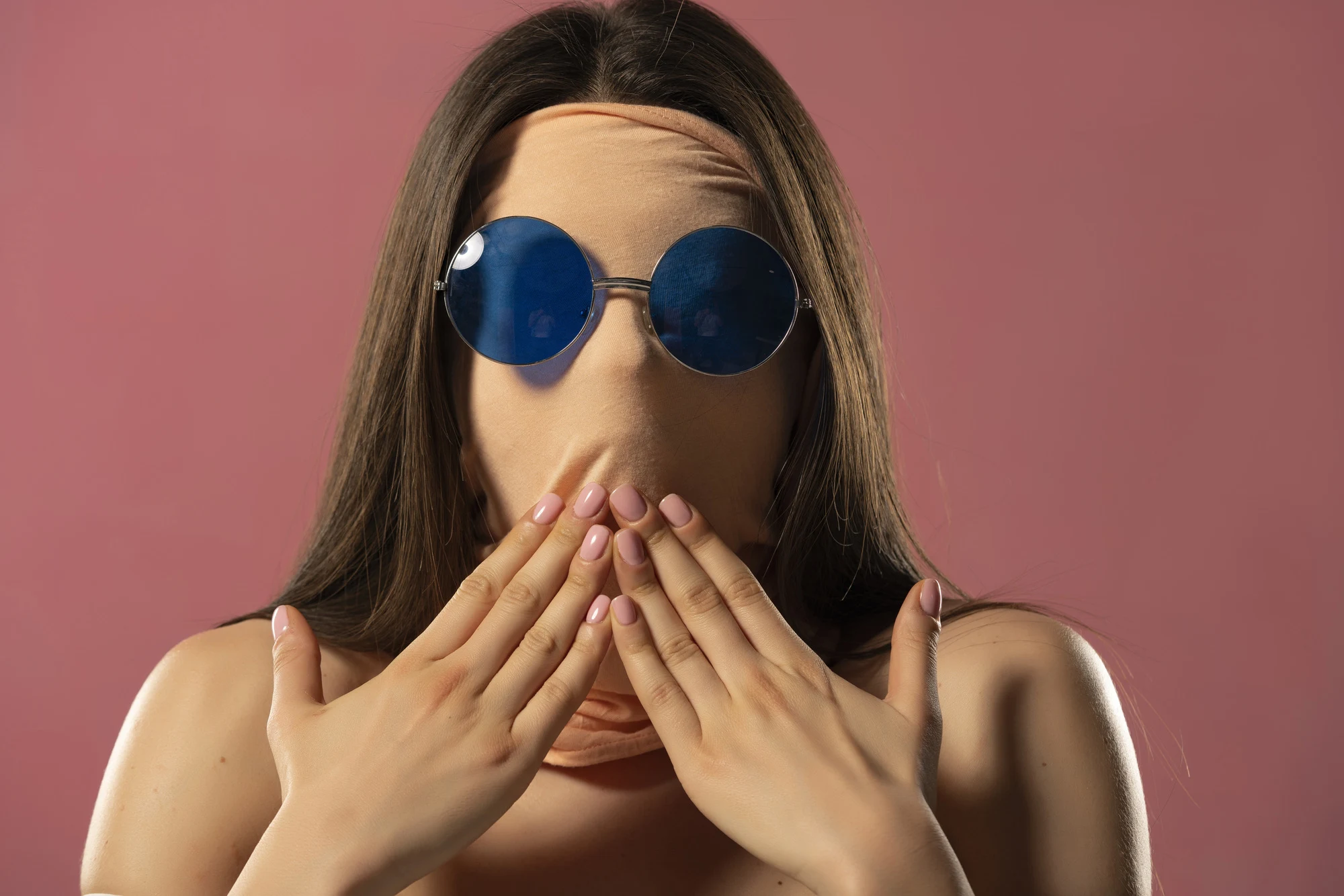 Portrait of unknown shocked woman with face wrapped in fabric wearing glasses on a pink colour background.