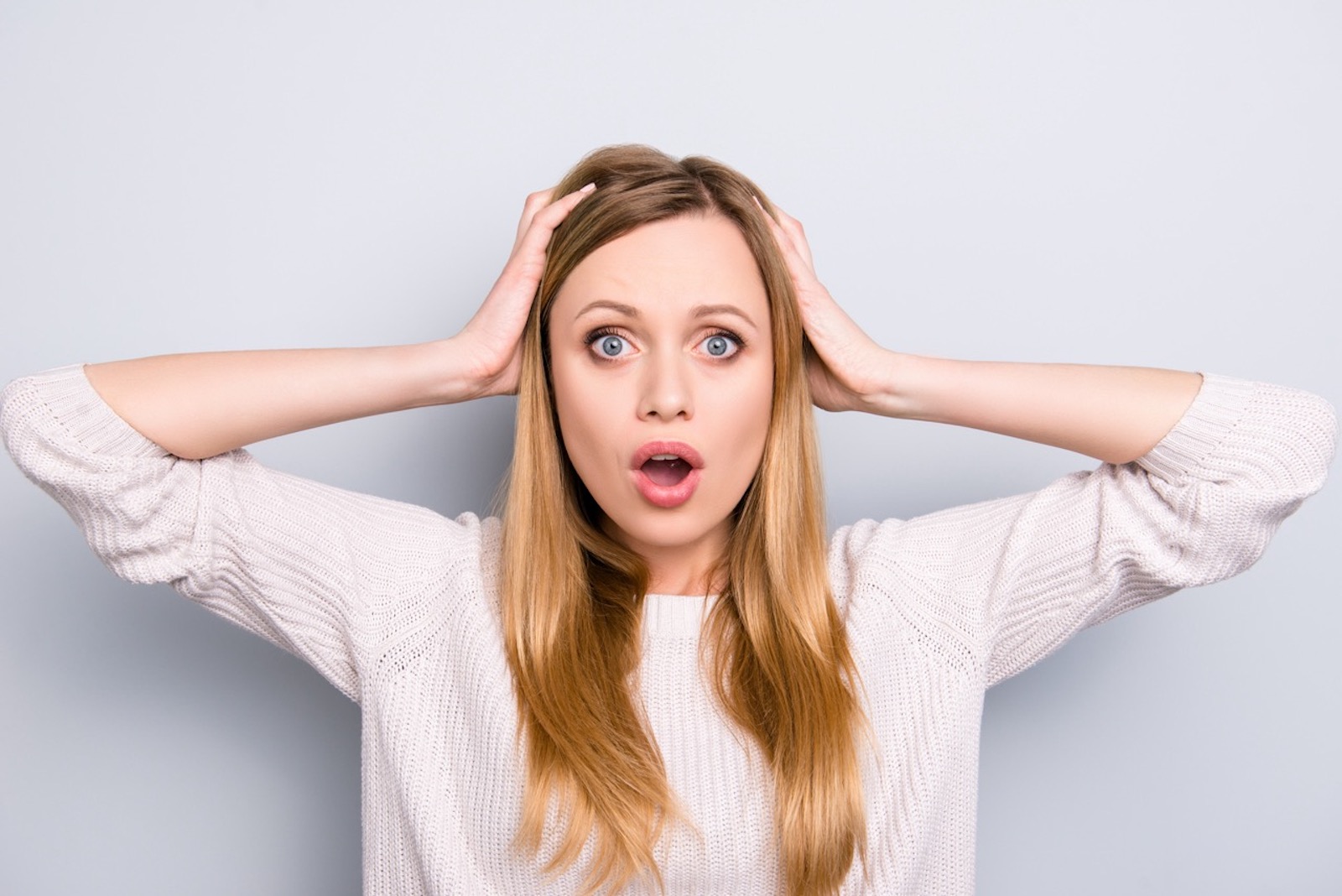 Portrait of curious frustrated girl with wide open mouth holding two hands on head looking at camera isolated on grey background