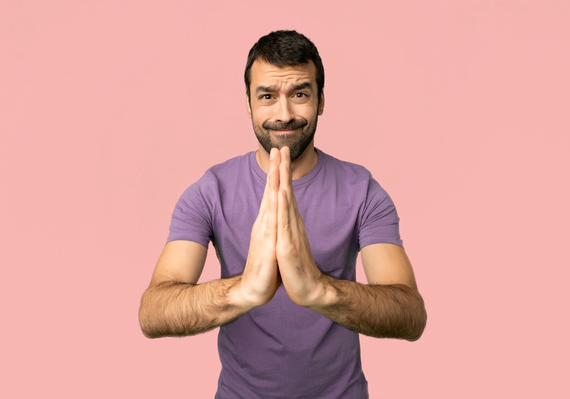 Handsome man keeps palm together. Person asks for something on isolated pink background