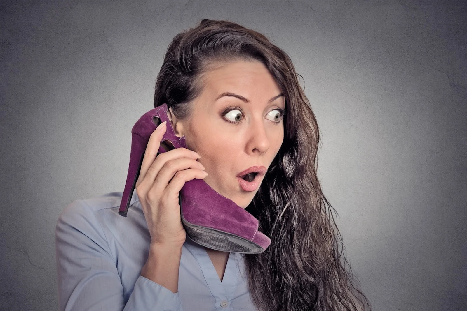 surprised woman holding high heeled shoe in hand as phone