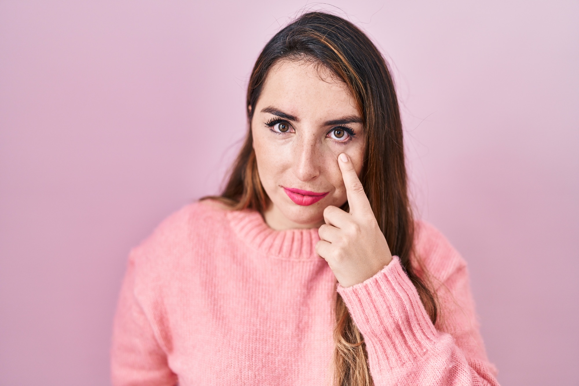 Young hispanic woman standing over pink background pointing to the eye watching you gesture, suspicious expression