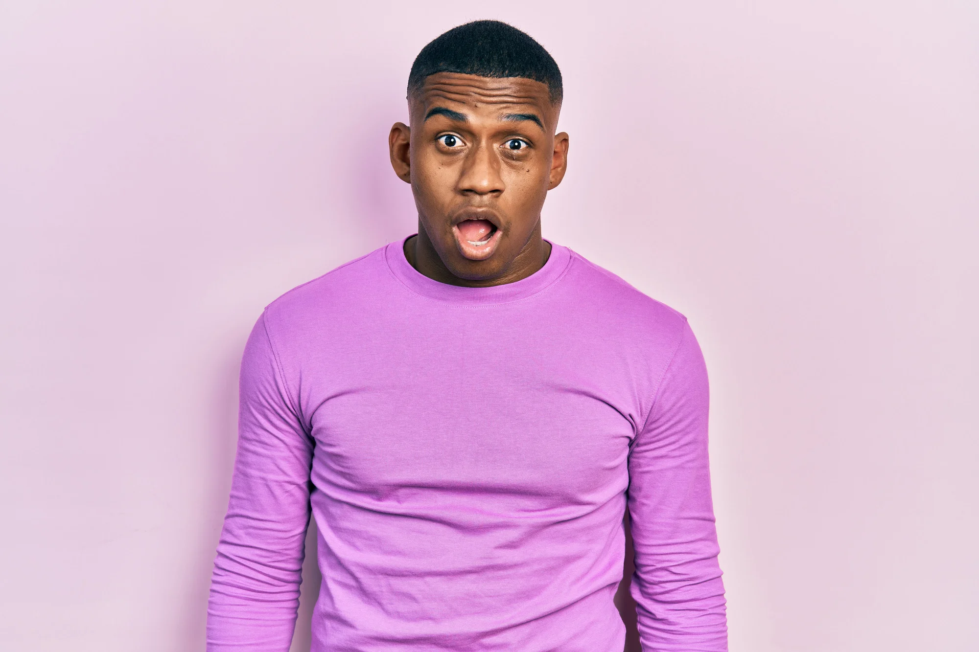 Young black man wearing casual pink sweater afraid and shocked with surprise and amazed expression, fear and excited face.