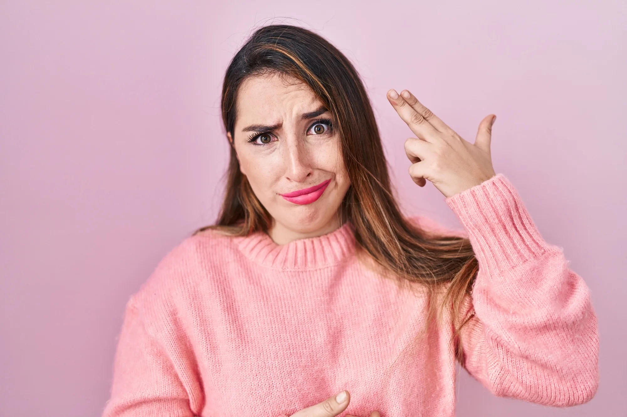 Young hispanic woman standing over pink background shooting and killing oneself pointing hand and fingers to head like gun, suicide gesture.