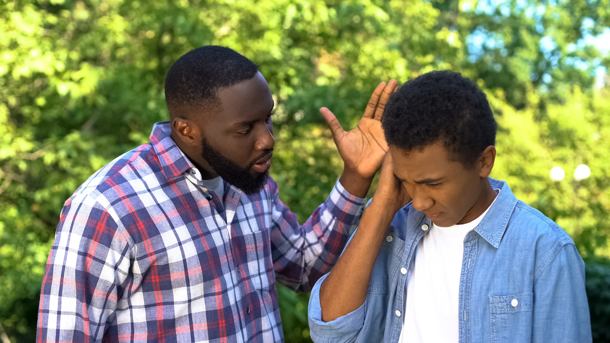 Angry male hitting son upside head shouting outdoors, parenting difficulties.