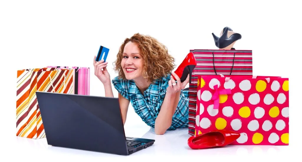 Happy young shopping woman with laptop, shopping bags holding a credit card and a red shoe - isolated