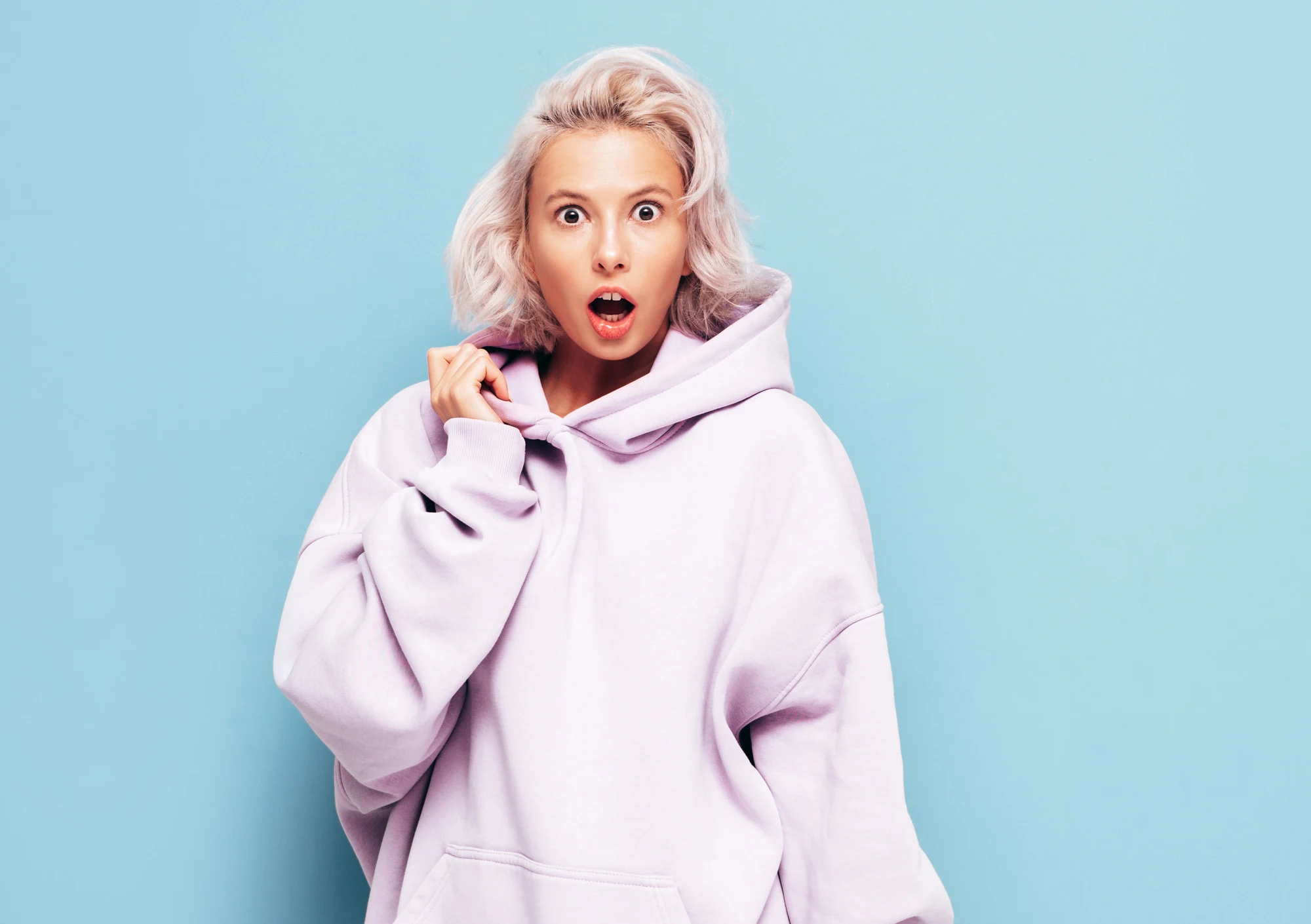 Portrait of young beautiful smiling female in trendy summer clothes. carefree woman posing near blue wall in studio. Positive blond model having fun and going crazy. Shocked and surprised