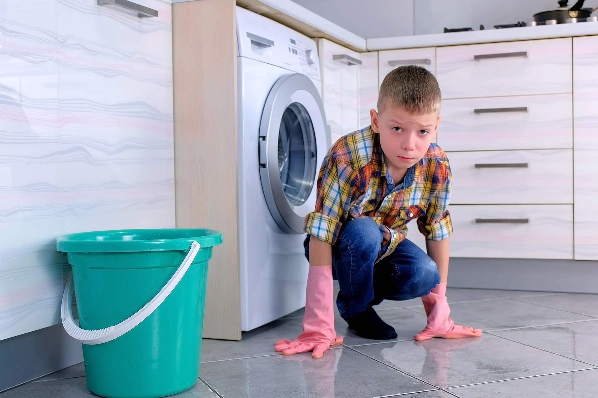 Tired boy in rubber gloves don't want to wash the floor in the kitchen. Child's home duties