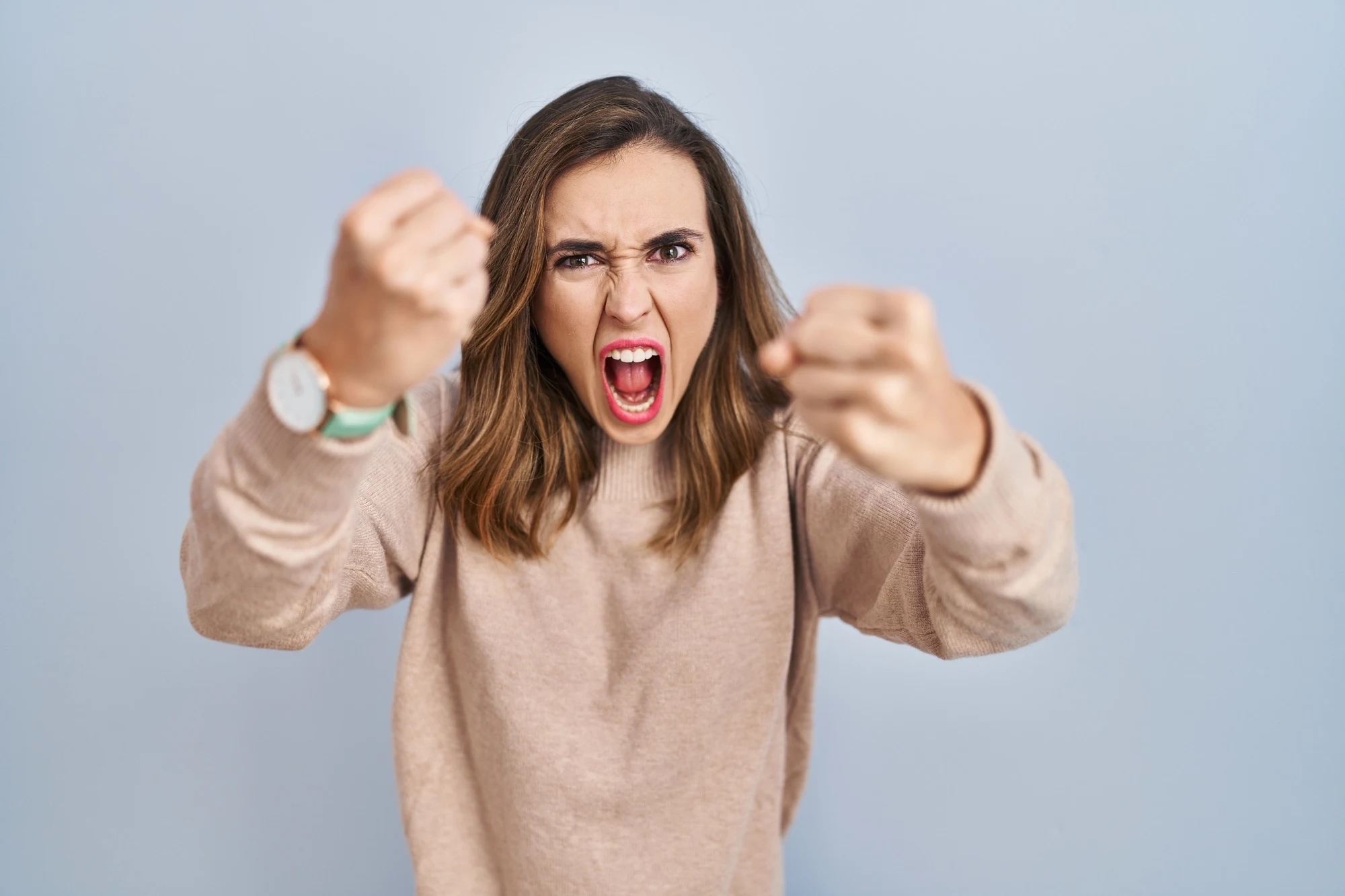 Young woman standing over isolated background angry and mad raising fists frustrated and furious while shouting with anger. rage and aggressive concept.