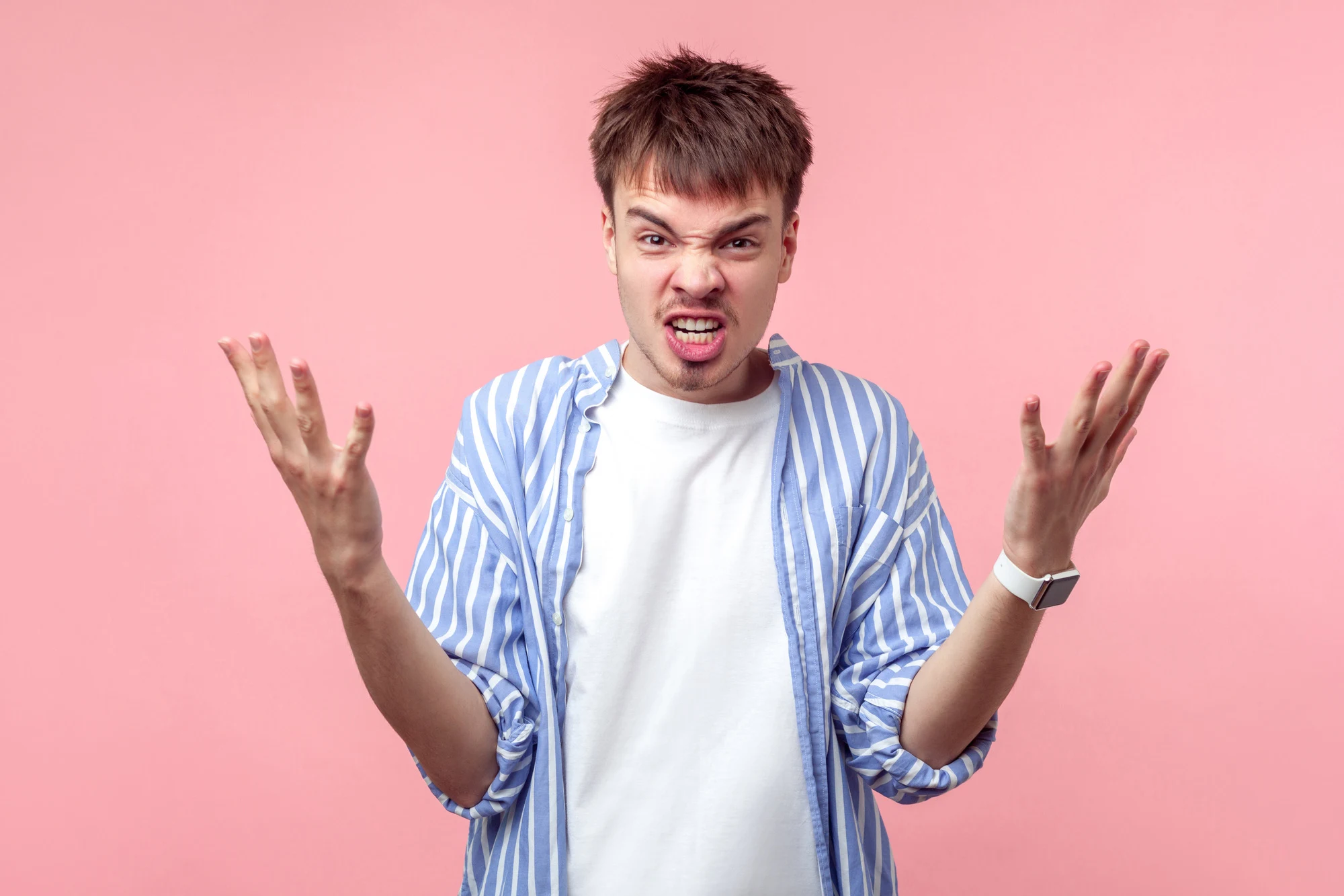 What do you want? Portrait of irritated brunette man with small beard and mustache in casual shirt raising arms in anger, asking why, furious expression. indoor studio shot isolated on pink background