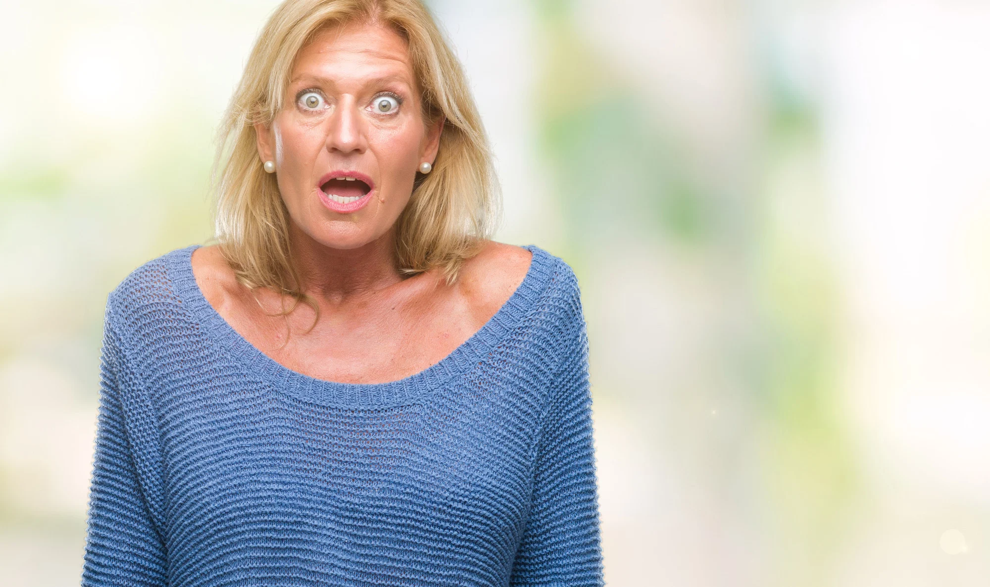 Middle age blonde woman wearing winter sweater over isolated background afraid and shocked with surprise expression, fear and excited face.