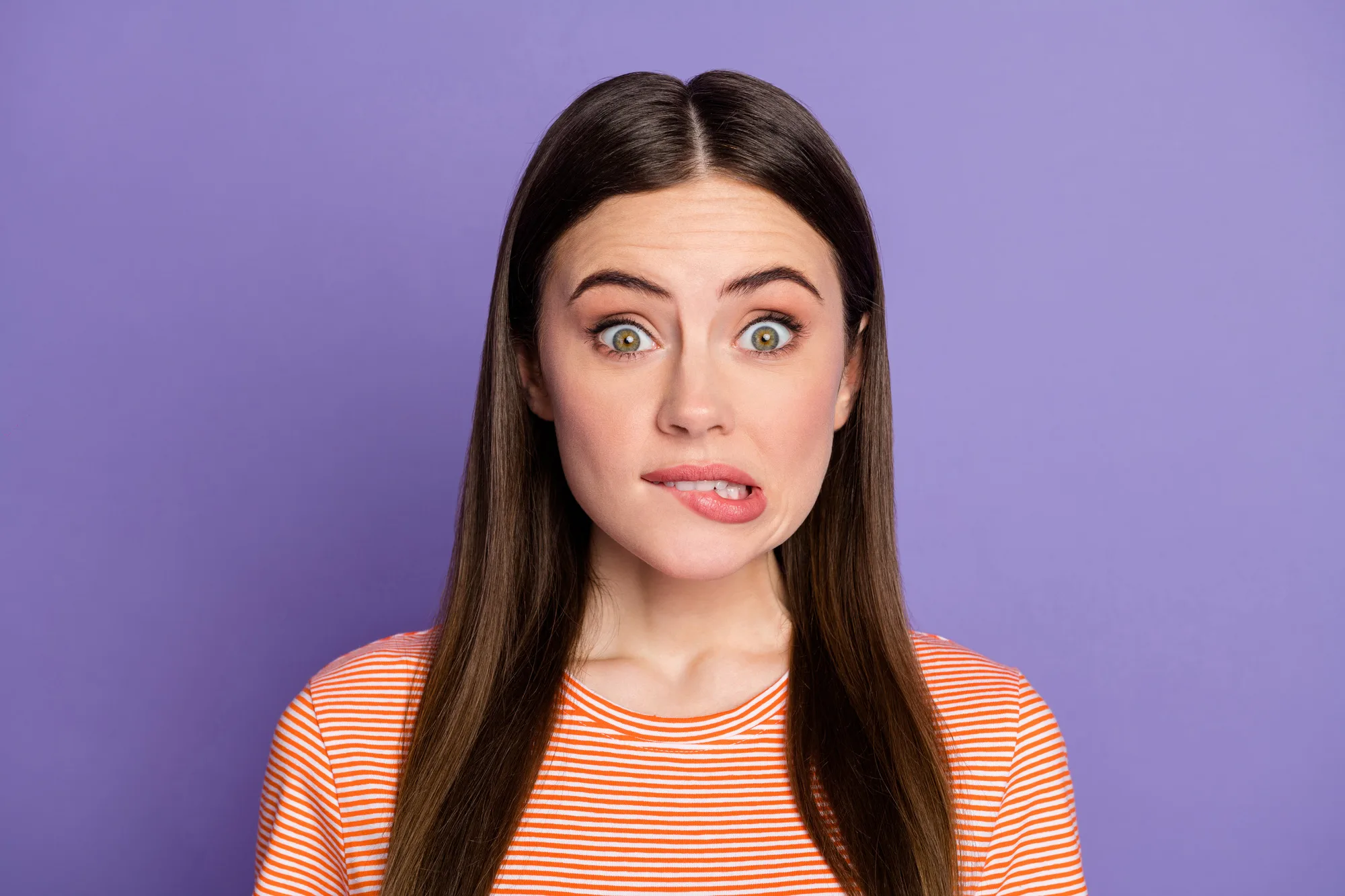 Closeup photo of attractive terrified lady biting lips made big mistake, eyes full of fear feel guilty wear casual orange striped t-shirt isolated pastel purple color background