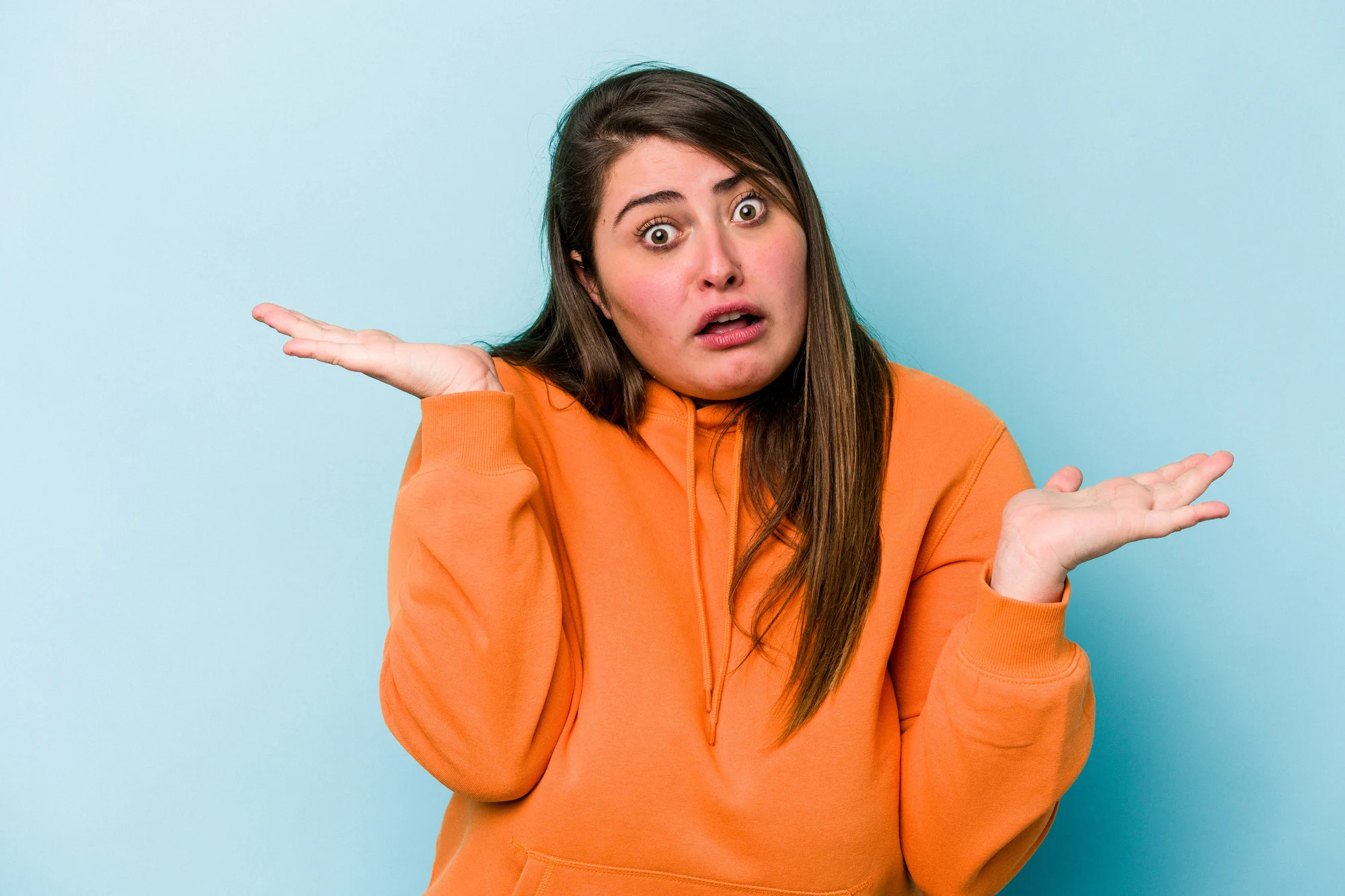 Young caucasian overweight woman isolated on blue background confused and doubtful shrugging shoulders to hold a copy space.