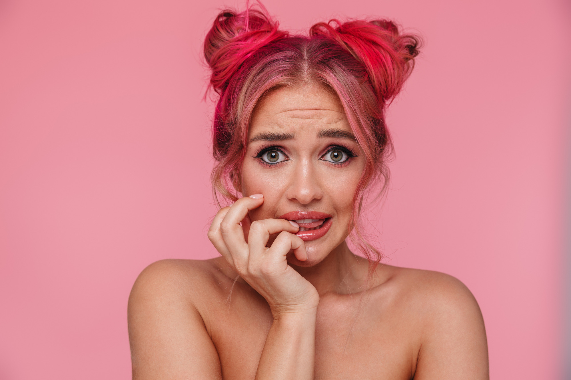 Portrait of uptight shirtless young woman with colorful hairstyle frowning and biting nails isolated over pink background