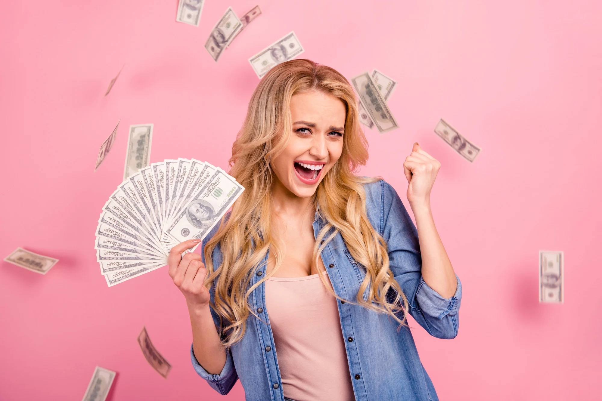 Pretty lady holding bucks bills flying, everywhere wear denim outfit isolated pink background