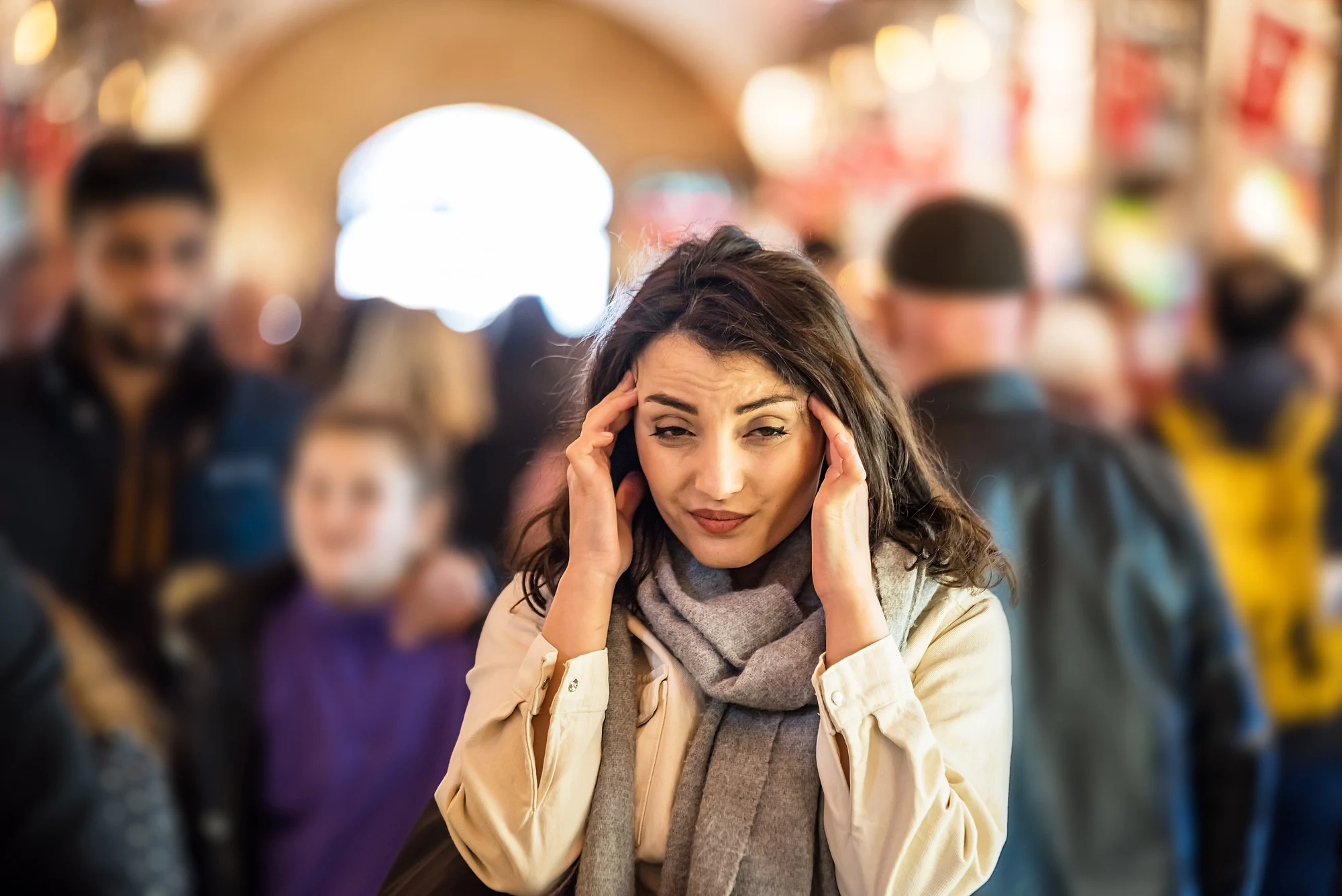 Beautiful woman in fashionable modern clothes suffers migraine or headache problem while standing crowd of people at road.