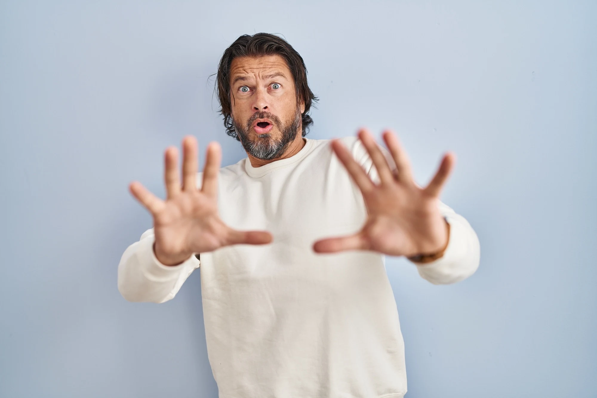 Handsome middle age man wearing casual sweater over blue background afraid and terrified with fear expression stop gesture with hands, shouting in shock. panic concept.