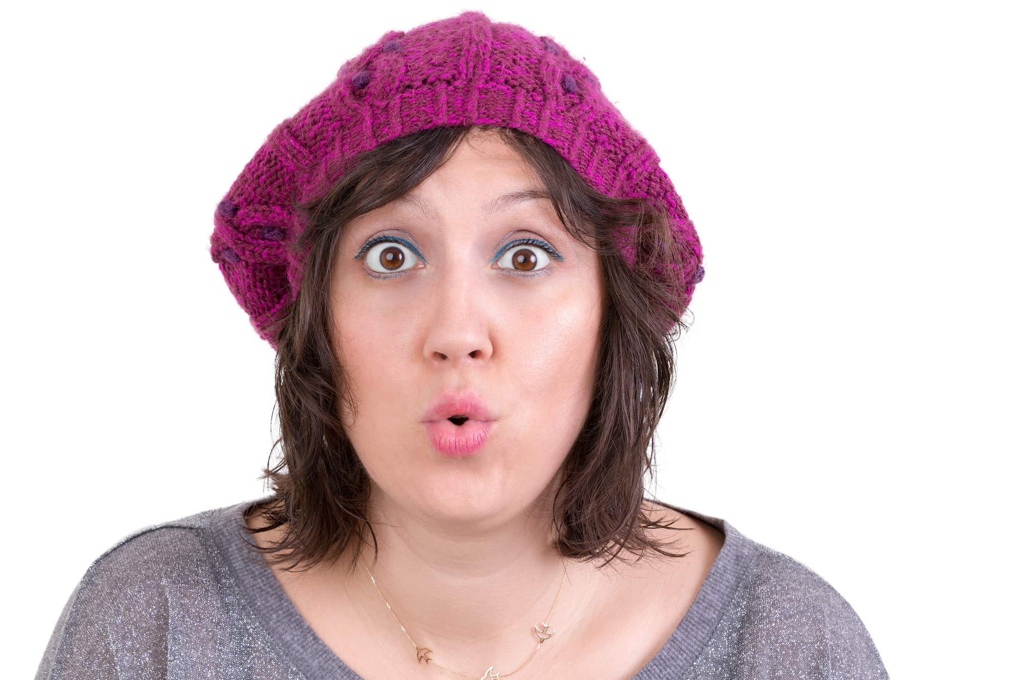 Woman wearing a purple knitted beanie reacting in amazement and wonder puckering her lips into an ooh expression with wide eyes, on white
