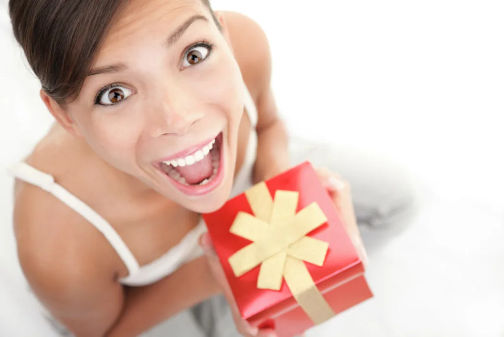 Happy excited woman holding gift / present. Cute surprised mixed Asian Chinese / Caucasian female model.