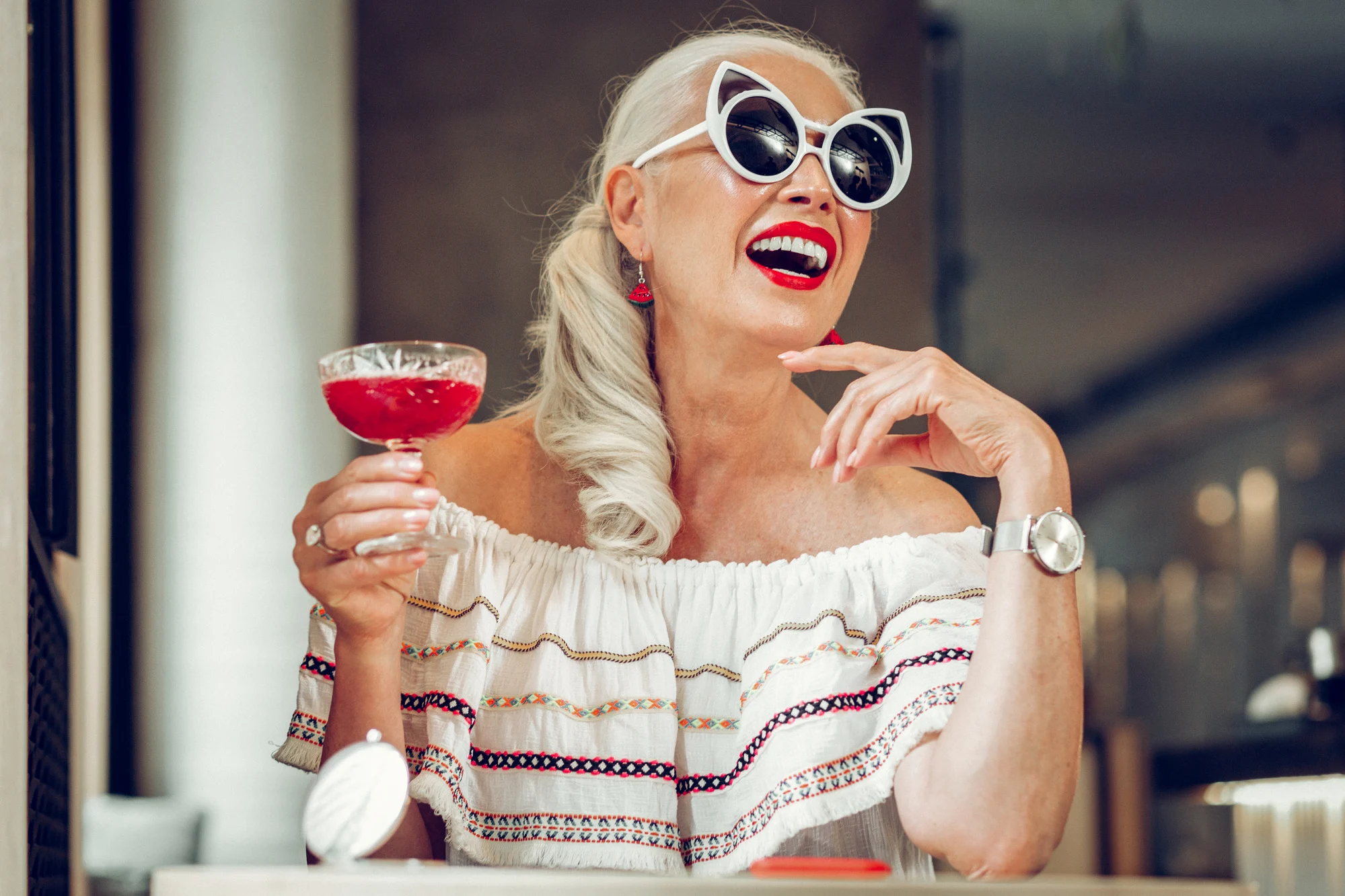 Sweet drink. Joyful nice woman enjoying her fancy cocktail while sitting with her drink at the table