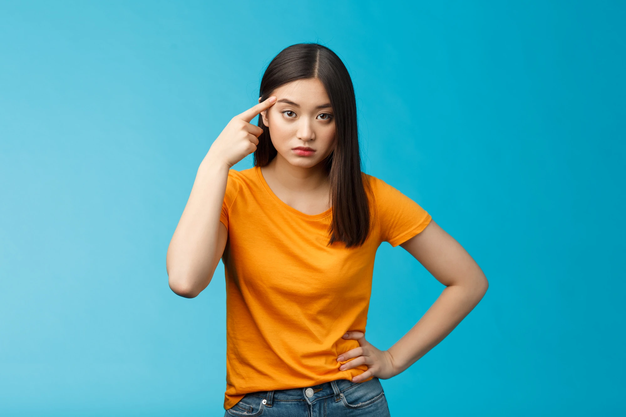 angry irritated asian girl look annoyed bend camera roll finger on temple stare camera bothered dismay, asking are you out mind, show person crazy weird, stand blue background. Copy space