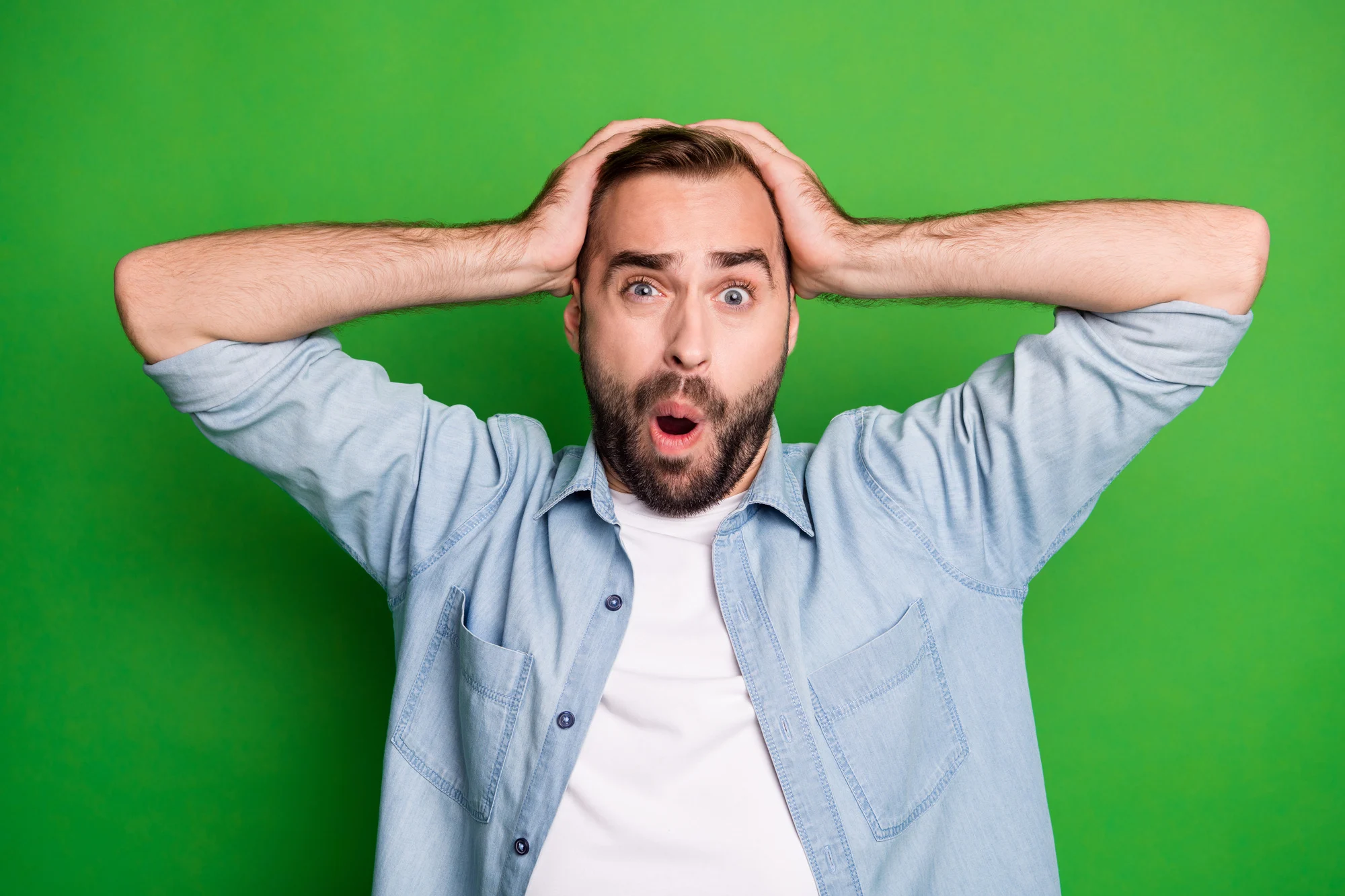 Portrait of impressed sad man wear blue shirt arm head open mouth isolated on green color background.