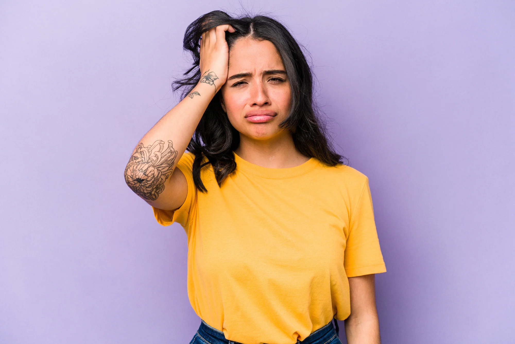 Young hispanic woman isolated on purple background tired and very sleepy keeping hand on head.
