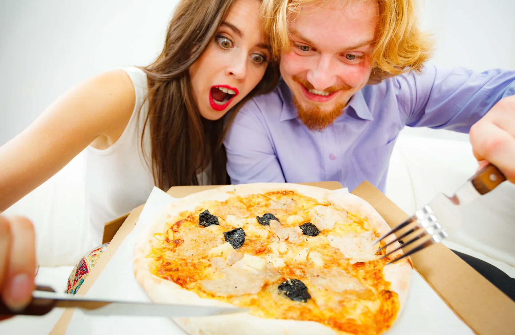Funny crazy man and woman spending time together. Cheerful couple or friends eating delicious cheesy pizza.