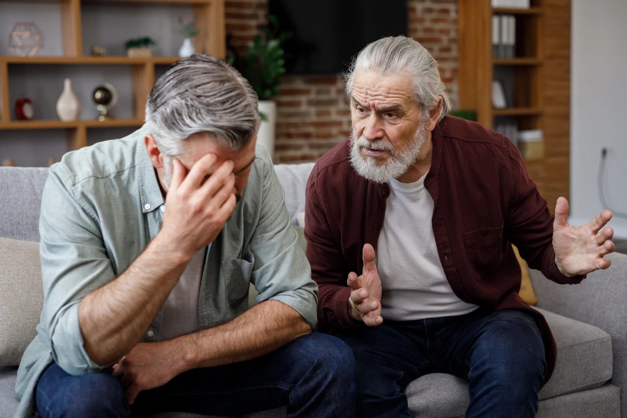 Family conflict. Adult son visiting senior father. Two generations family has unpleasant conversation sitting on couch at home. Generational confrontation