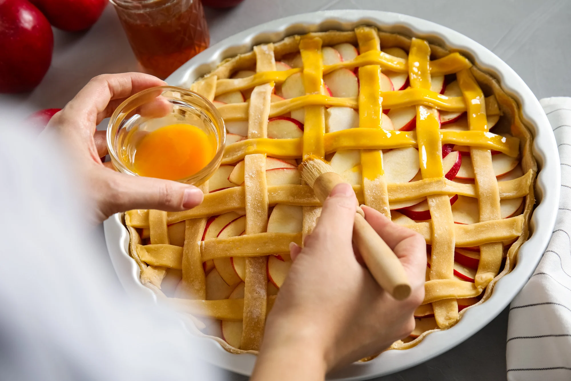 Woman applying liquid egg onto traditional English apple pie with brush at table, closeup