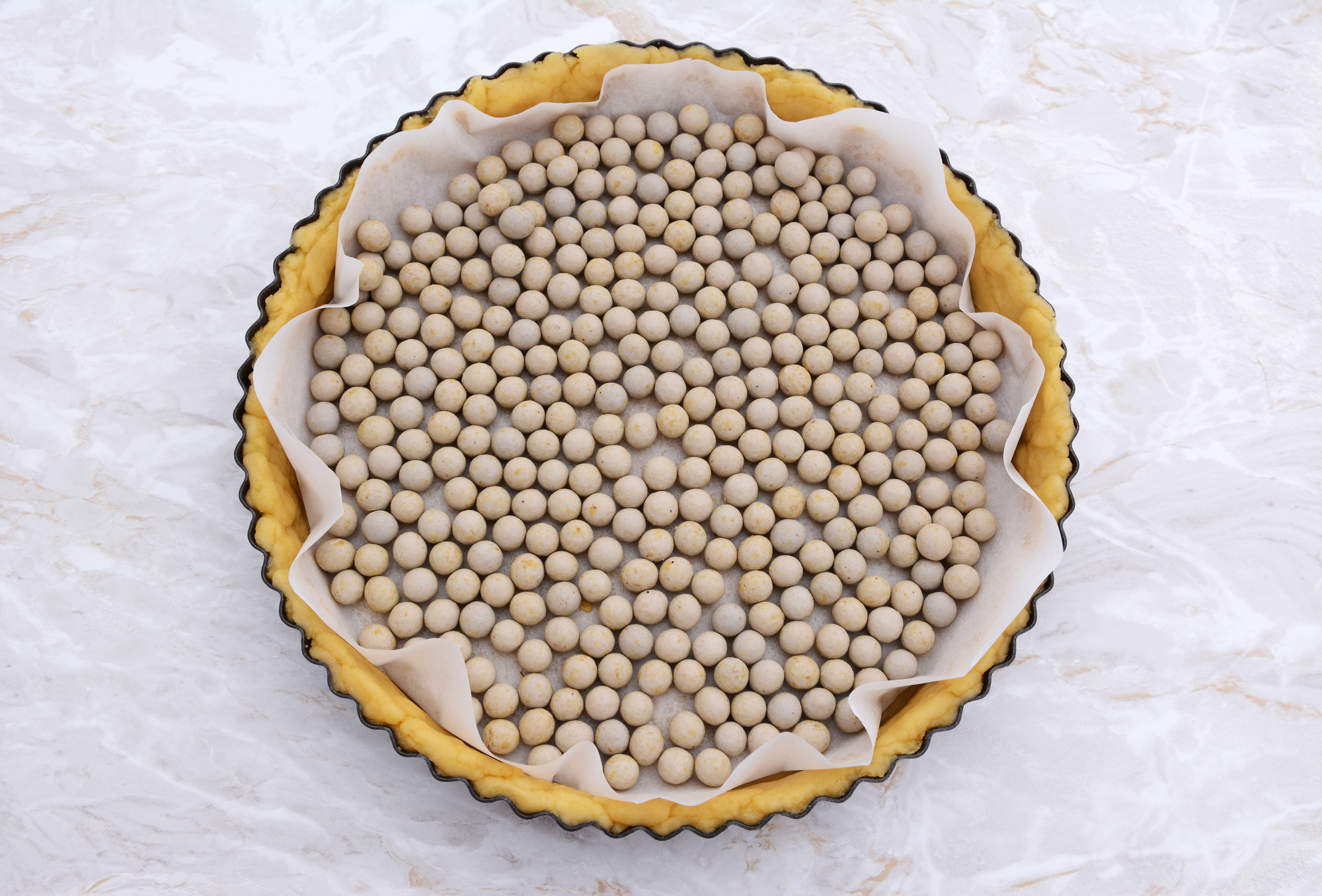 Ceramic beans used as pastry weights in an uncooked pie crust lined with greaseproof paper