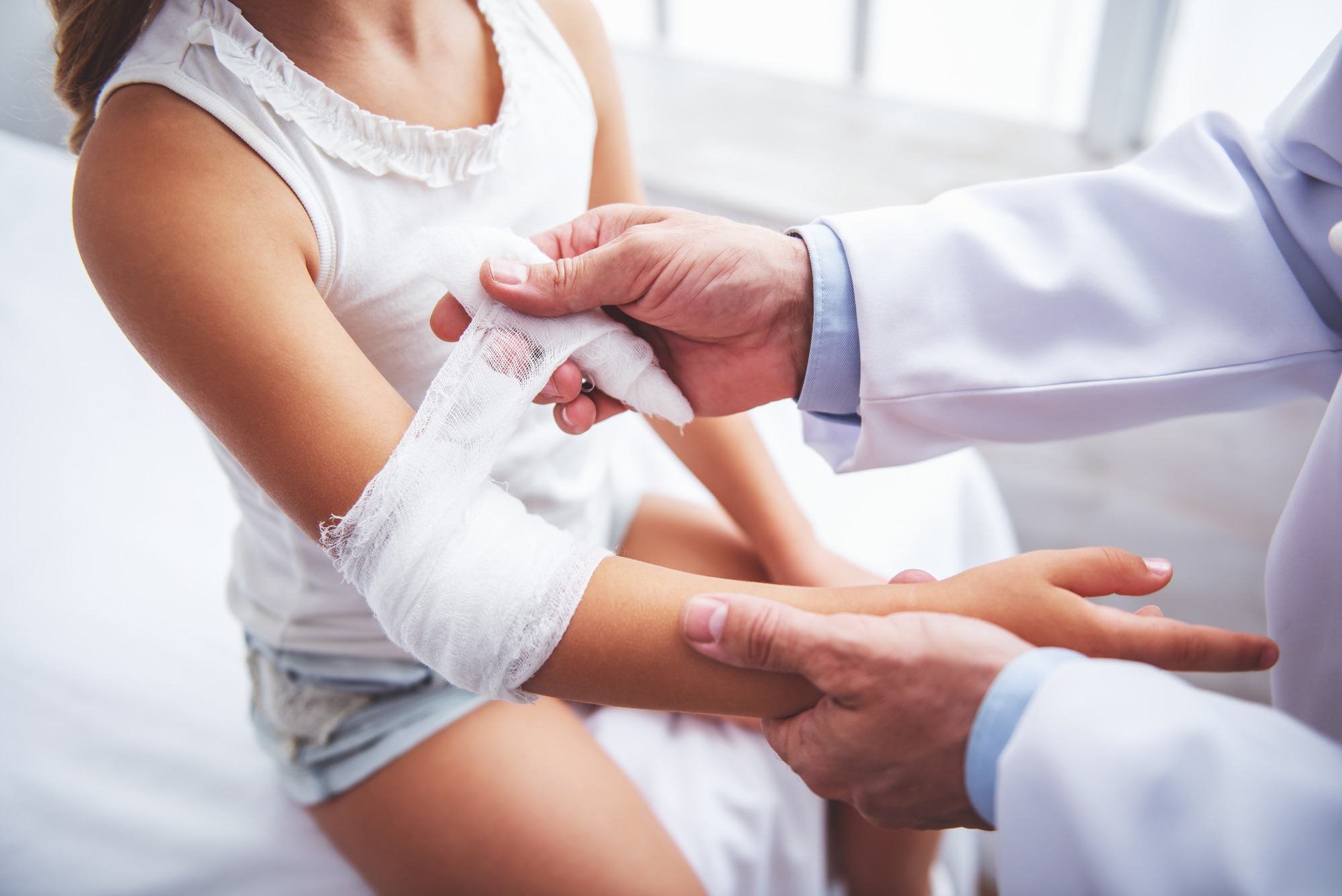 Handsome middle aged pediatrician is putting a bandage on little girl arm, close-up